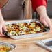 A person holding a Western Plastics foil steam table pan filled with food.