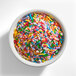 A white bowl filled with colorful rainbow sprinkles.