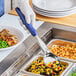 A person in gloves using a Vollrath blue round portion spoon to serve mixed vegetables.