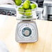 A hand holding a bowl of limes on a Taylor portion scale on a counter.