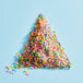 A triangle of Adourne Mini Pastel Confetti Sprinkles with many small round candies on a blue background.