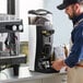 A man in an apron using a Gaggia G10 white espresso grinder on a counter in a coffee shop.