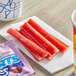 A white cup of SweeTarts Cherry Punch Ropes next to a group of red sticks.