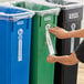 A person putting a label on a green and blue recycling bin.