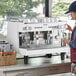 A woman using a Gaggia Vetro espresso machine to make coffee with metal mugs.