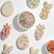 A bowl of mini pastel confetti sequin sprinkles surrounded by decorated sugar cookies.