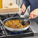 A woman cooking food in a Vollrath Wear-Ever non-stick fry pan.