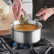 A person pouring food into a Vollrath Tribute stainless steel sauce pan on a stove.