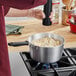 A person pouring sauce into a red Vollrath sauce pan on a stove.