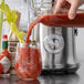 A person pouring red juice into a glass from a Breville juice extractor.