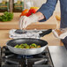 A person in gloves pouring seasoning on food in a Vollrath Wear-Ever non-stick fry pan.