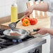 A person cooking a piece of meat in a Vollrath Wear-Ever aluminum fry pan on a stove.