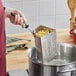 A person using a Vollrath stainless steel pasta basket to cook pasta in a pot.