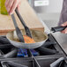 A person cooking food in a Vollrath Wear-Ever non-stick fry pan.