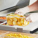 A person in gloves holding a clear polycarbonate food pan of yellow squash.