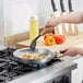 A person using a Vollrath Wear-Ever aluminum fry pan to cook food on a stove.