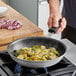 A person cooking brussels sprouts and onions in a Vollrath Wear-Ever non-stick fry pan.