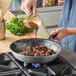 A person pouring sauce into a Vollrath Wear-Ever non-stick fry pan of meat.