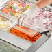 A gloved hand uses a Choice clear polycarbonate lid to cover a plastic container of carrots.