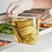 A person in gloves holding a clear plastic food pan filled with pickles.