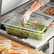 A person in gloves using a Choice clear polycarbonate food pan lid with a handle to cover a container of food on a counter.