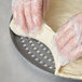 Plastic gloved hands making dough on an American Metalcraft Super Perforated Pizza Pan.