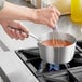 A person stirring sauce in a Vollrath stainless steel sauce pan on a stove.