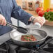 A person cooking meat in a Vollrath stainless steel fry pan.