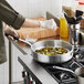 A person cooking brussels sprouts in a Vollrath Wear-Ever saute pan on a stove.