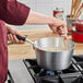 A person stirring food in a Vollrath Wear-Ever sauce pan on a stove.