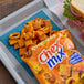 A bag of Cheddar Chex Mix snack mix with some of the mix poured out onto a blue napkin on a tray.