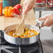 A person cooking food in a Vollrath Wear-Ever aluminum saute pan with a wooden spatula.