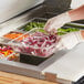 A person in gloves using a Choice clear plastic food pan to hold onions.