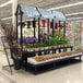 A Benchmaster black plastic three step display with a plant hanger holding green plants in a store.