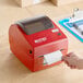 A hand using a DayMark Matt85 thermal label printer to print a label.