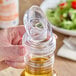 A hand using a Cal-Mil no-drip pour lid to pour olive oil into a bottle on a table.