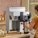 A woman using a Fetco CBS-1232 coffee machine on a counter in a coffee shop.