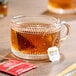 A clear glass cup filled with Twinings English Breakfast decaffeinated tea, with a tea bag and packet visible nearby.