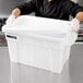 A man in a chef's uniform and gloves holding a white Rubbermaid tote with a lid.