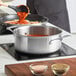 A woman using a Vigor stainless steel stock pot to cook food.