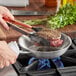 A person cooking a piece of meat in a Vigor stainless steel fry pan.