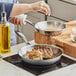 A person cooking meat in a Vigor stainless steel fry pan.