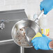 A person in blue gloves cleaning a Vigor stainless steel fry pan with a yellow sponge.