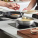 A person pouring sauce from a metal spoon into a Vigor Tri-Ply Stainless Steel Saucier Pan.