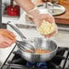 A person using a Vigor SS3 Series saucier pan to stir food on a stove.