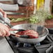 A person cooking meat in a Vigor stainless steel fry pan on a stove.