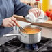 A person using a Vigor stainless steel sauce pan to stir food on a stove.