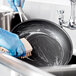 A person in blue gloves cleaning a Vigor stainless steel non-stick fry pan with a brush.