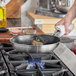 A person using a Vigor SS3 Series stainless steel non-stick fry pan to cook meat on a stove.