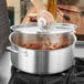 A person using a Vigor stainless steel brazier to cook food on the stove.